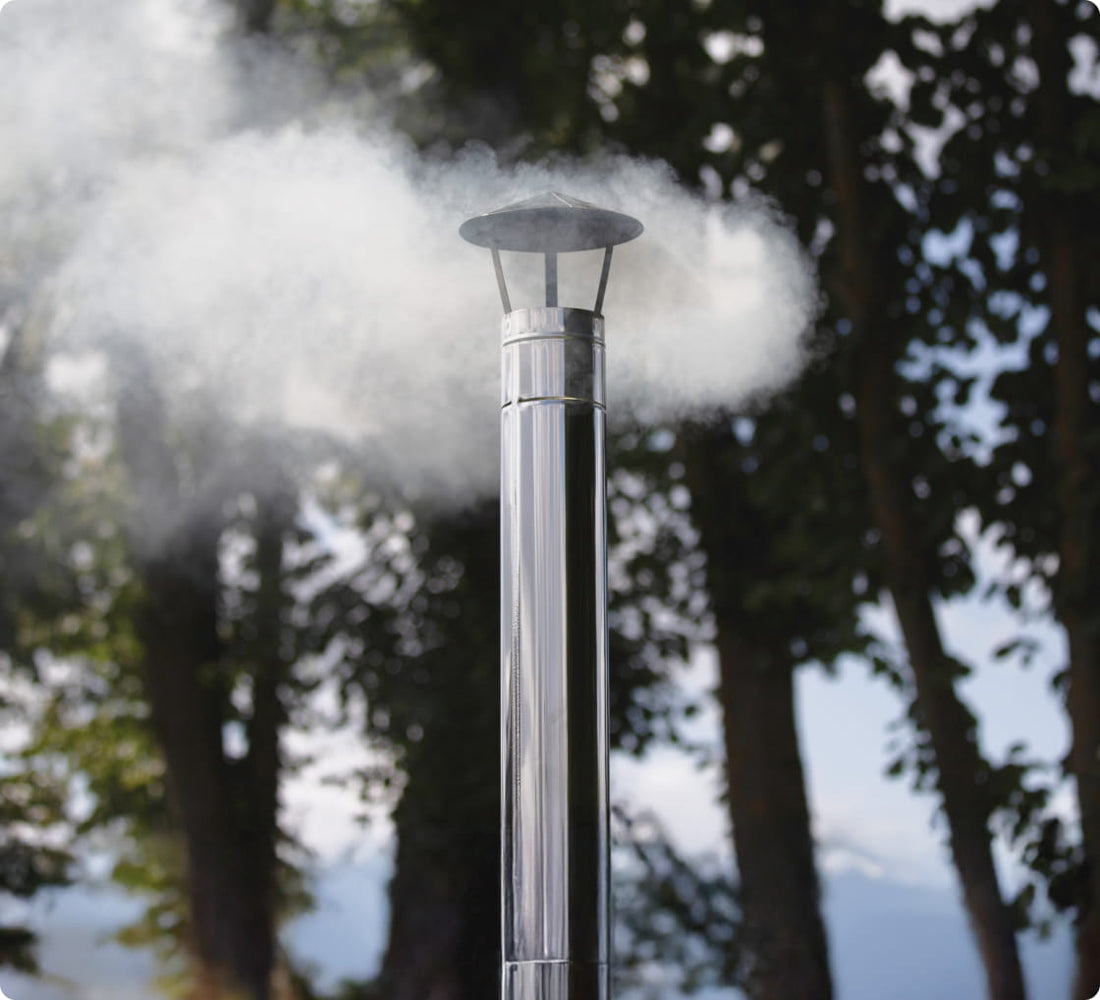A chimney extension with smoke rising from it, surrounded by trees