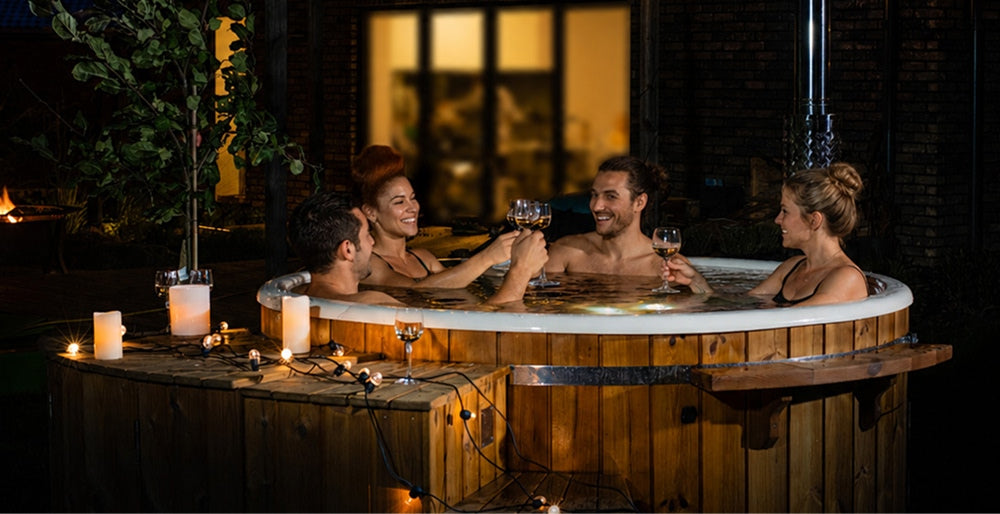 Vier Freunde entspannen an einem dunklen Abend in einem Hot Tub und erheben ihre Gläser im romantischen Licht.