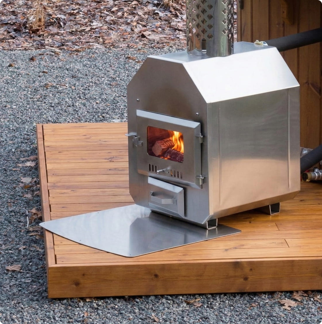 Stainless steel outdoor external wood stove on a ash plate with fire burning inside.