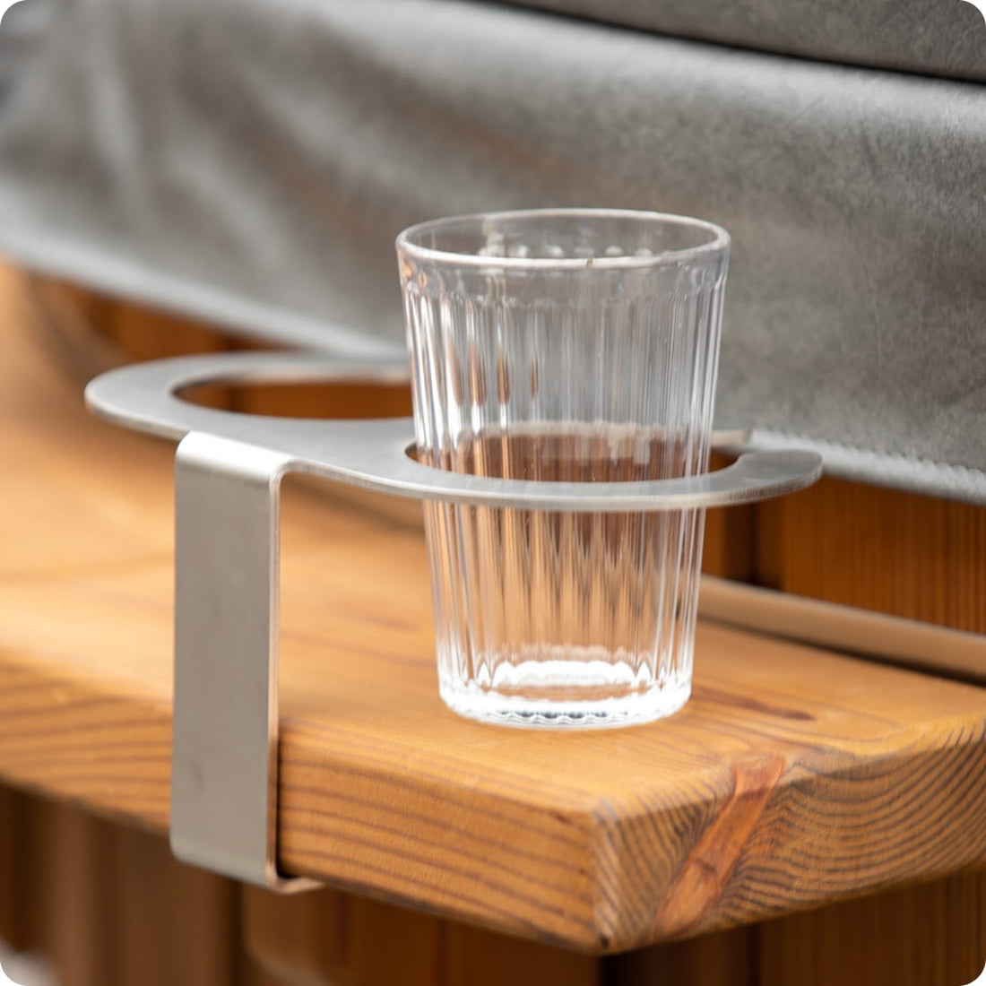 Clear glass cup on a metal holder attached to a wooden surface with a gray cover in the background.