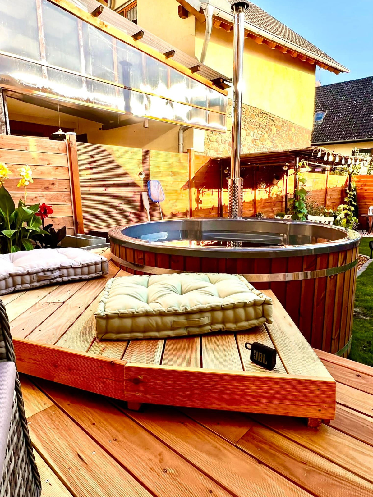 Gardenvity Holzofen-hot tub auf erhöhter Holzterrasse mit Kissen und moderner Gartendekoration.