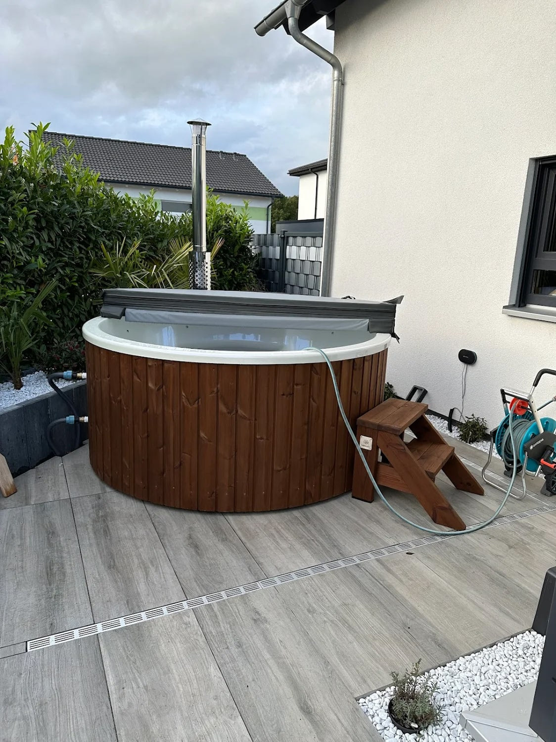 Gardenvity Holzofen hot tub auf einer gefliesten Terrasse neben einem modernen Haus installiert.