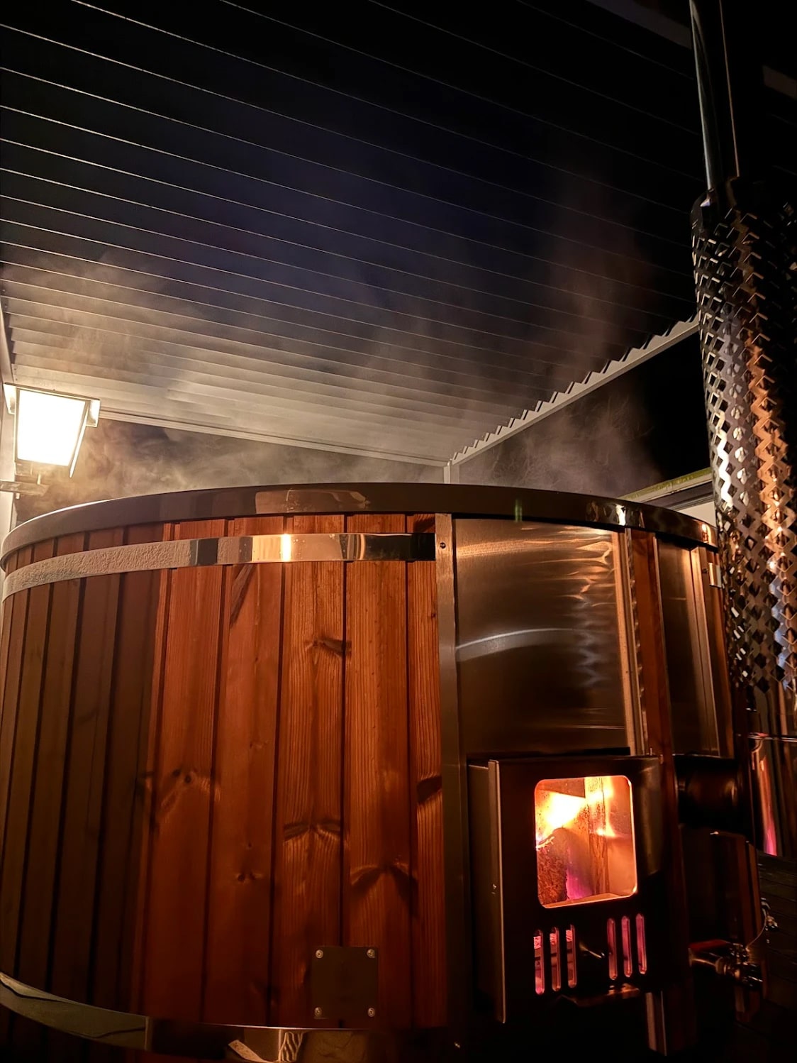 Steam rising from Gardenvity wood fired hot tub with fire burning inside stainless steel stove.