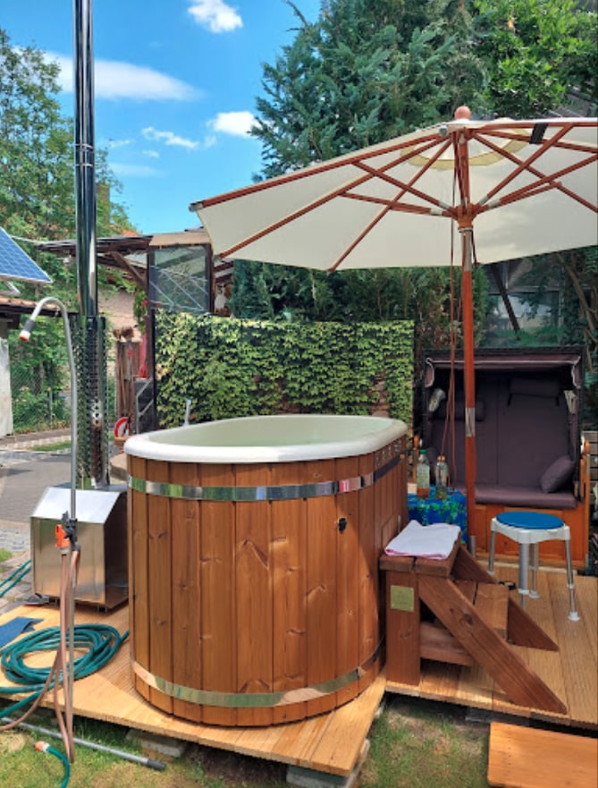 Gardenvity wood fired hot tub with white insert beside patio umbrella in sunny backyard garden.