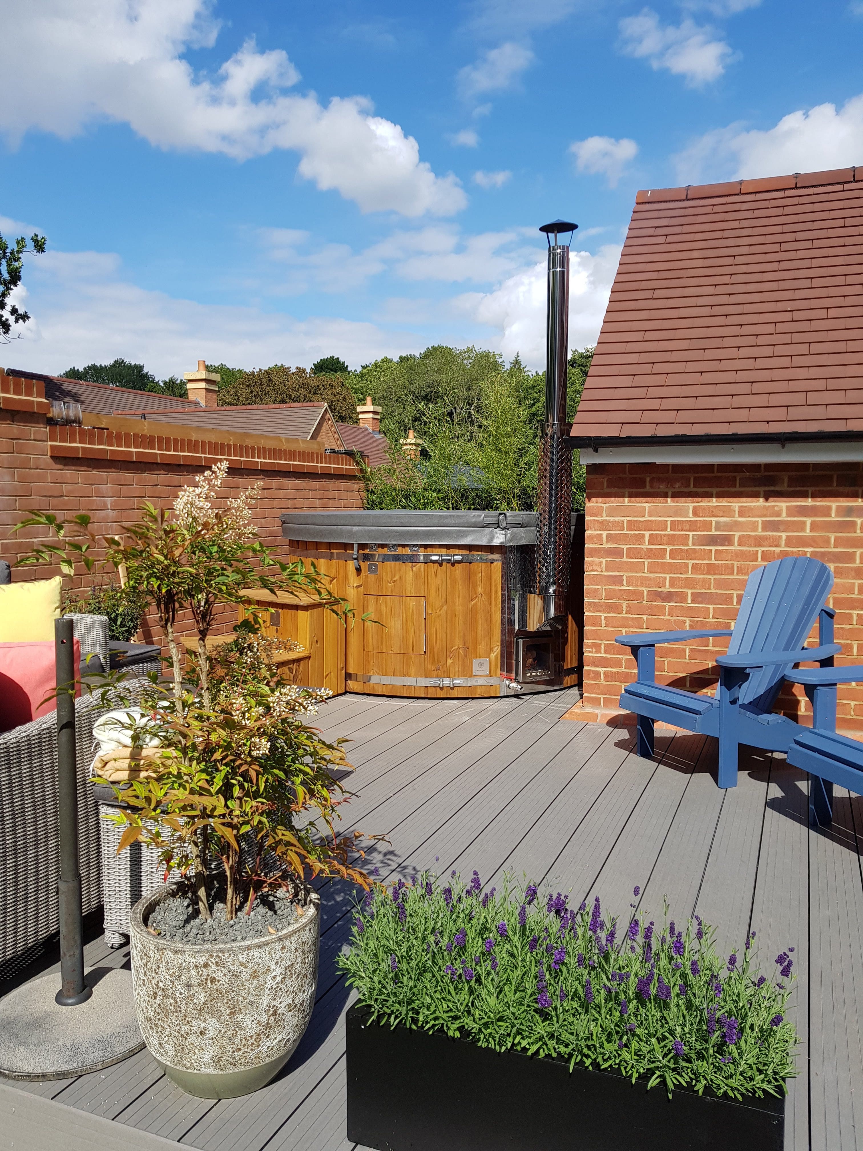Gardenvity wood fired hot tub on a small wooden deck between houses with cozy seating area.