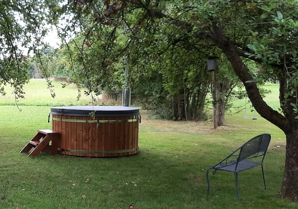 Gardenvity wood fired hot tub placed in open green field surrounded by trees and nature.