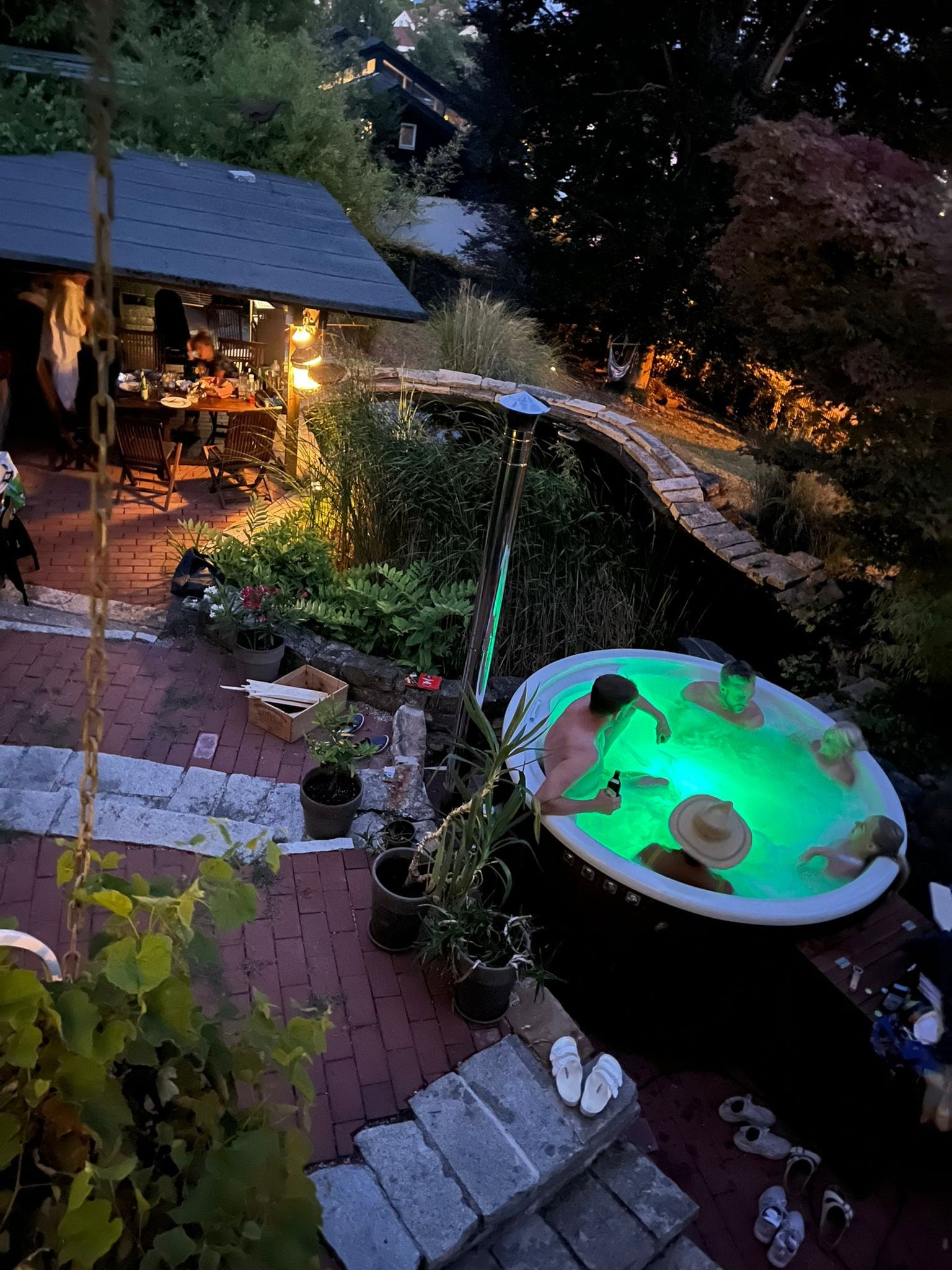 Gardenvity wood fired hot tub illuminated with green lights in evening backyard garden.