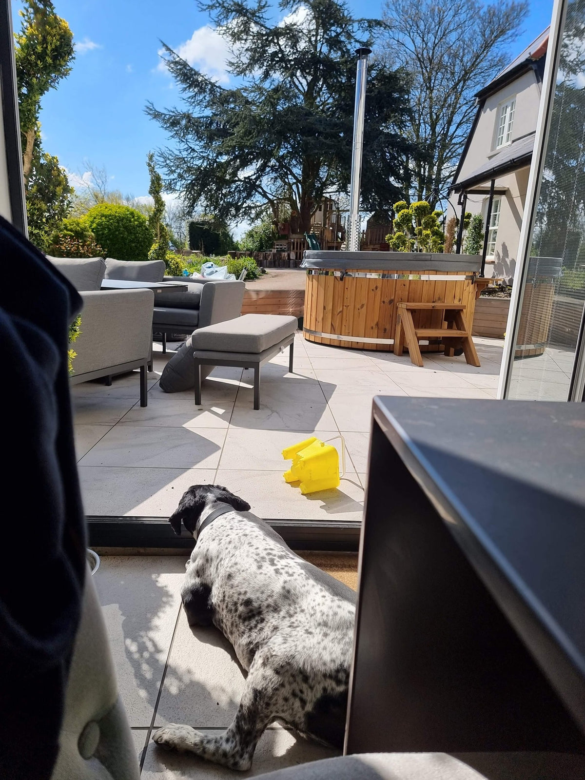 Gardenvity Holzofen-hot tub auf einer modernen Terrasse mit Gartenmöbeln und Hund in Sichtweite.