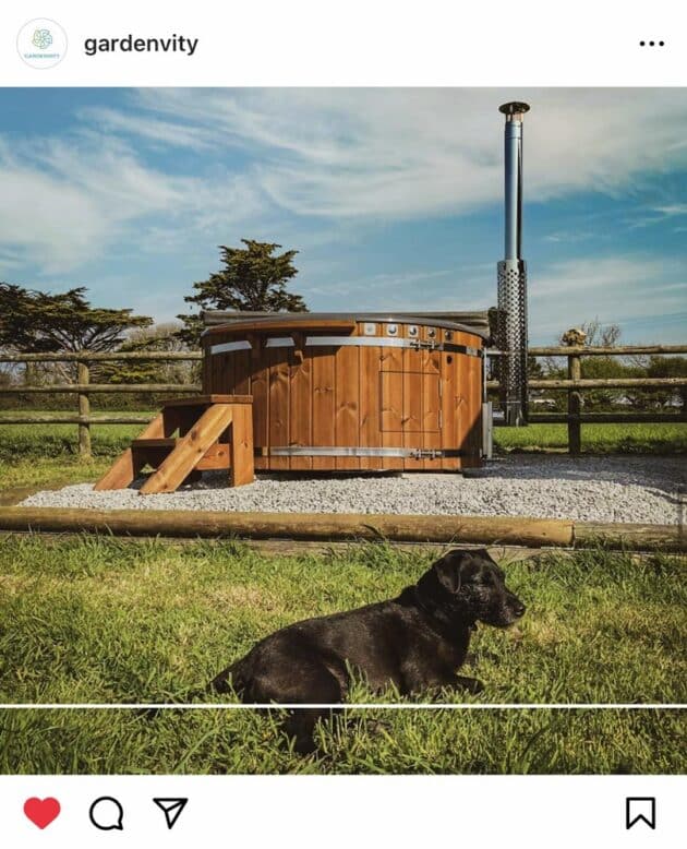 Ein holzbefeuertes Badezuber von Gardenvity, bewacht von einem Hund.